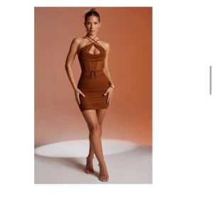 Brun kort klänning med snörning - Snygg brun kort klänning med korsade axelband och cut out-detalj framtill. Klänningen har snörning i midjan och är figurnära med rynkade sidor. Perfekt för dig som vill sticka ut med en trendig look. Har 2 stycken av den varav ena har kvar prislapp 