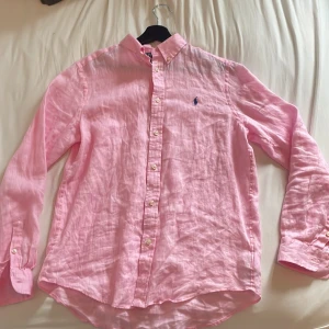 Rosa linneskjorta från Polo Ralph Lauren - Säljer en rosa skjorta från Polo Ralph Lauren i 100% linne. Skjortan har klassisk krage, knäppning framtill och lång ärm. Broderad blå logga på bröstet ger en clean och stilren look. Helt ny ock oanvänd🌟🌟🌟
