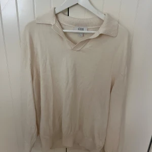 Beige tröja med krage från COS - Stilren beige tröja från COS med snygg krage och v-ringning. Tillverkad i en mjuk mix av 85% bomull och 15% siden. Tröjan har långa ärmar och ribbade muddar vid ärmslut och nederkant. Perfekt för dig som gillar minimalistisk och clean stil. Är storlek XL, men är mer en L skulle jag säga i passform 