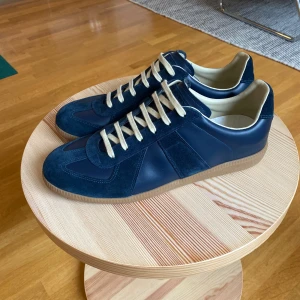 Maison Margiela sneakers blå mocka - Maison Margiela gat sneakers i mörkblå mocka och skinn med beige snörning och gummisula. Klassisk low-top modell med stilren design och diskreta detaljer. !! KVITTO FINNS!! Skriv för fler bilder eller frågor🙌