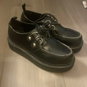 Svarta platåsneakers med nitar från Lamoda - Säljer ett par svarta sneakers från Lamoda med chunky platåsula, silvriga nitar längs hälen och snörning framtill. Skorna har detaljer i metall och en cool, edgy vibe. Perfekta för dig som vill sticka ut med din stil.