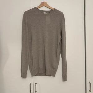 Beige merinoulltröja från Cubus - Snygg beige rundhalsad tröja från Cubus i 100% merinoull. Den har en klassisk passform med långa ärmar och ribbade muddar vid ärmslut och nederkant. Perfekt för lager-på-lager under höst och vinter.