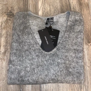 Grå v-ringad tröja från Vero Moda - Mysig ljusgrå melerad tröja från Vero Moda med v-ringning och långa ärmar. Perfekt för lager-på-lager och chill dagar. Tröjan är i mjukt material och har en avslappnad passform som funkar till allt.