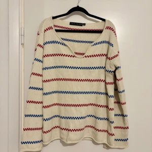 Randig stickad tröja från Palladium pippitröja - Vit stickad tröja från Palladium med röda och blå horisontella ränder. Tröjan har v-ringning, ribbad struktur och långa ärmar. Perfekt för dig som gillar en avslappnad och snygg stil med lite retrovibbar.