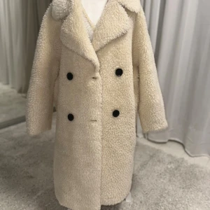 Beige teddyjacka med stora slag - Säljer en oversized beige teddyjacka med stora slag och dubbelknäppning med svarta knappar. Jackan har fickor på sidorna och är gjord i mjukt, fluffigt material som håller dig varm hela vintern. Helt ny aldrig använd 