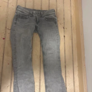 Grå raka jeans från Pepe Jeans - Snygga grå jeans från Pepe Jeans i utsvängd modell med låg midja. Jeansen har klassisk femficksdesign och är tillverkade i en mjuk bomullsblandning med lite stretch för extra komfort. Perfekta för dig som gillar en avslappnad och stilren look.