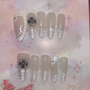 M - orm-mönster och kors - Snygga lösnaglar i nude med vitt orm-mönster och detaljer som små svarta kors och ormansikten. Naglarna är långa och spetsiga, och har en cool, edgy vibe. Perfekt för dig som vill sticka ut med unika naglar.