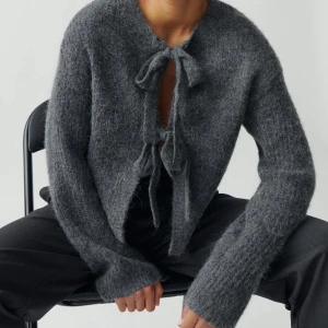 Mörkgrå stickad kofta med knyt - Mysig mörkgrå stickad kofta från Gina Tricot med långa ärmar och knytband framtill vid halsen. 