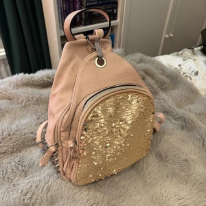 Rosa ryggsäck med paljetter och nitar - Säljer en superfin ljusrosa ryggsäck med glittriga guldpaljetter på frontfickan och coola silvriga nitar på sidan. Perfekta detaljen för festival!!