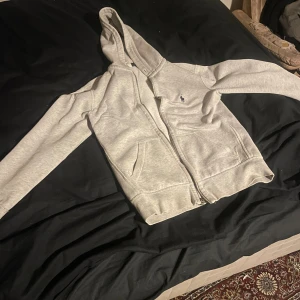 Grå hoodie från Polo Ralph Lauren - Snygg grå hoodie från Polo Ralph Lauren med klassisk logga broderad på bröstet. Tröjan har huva, dragkedja framtill och två stora fickor. Perfekt för chill dagar och enkel att matcha med jeans eller joggers. Hoodien har tappat snöret.