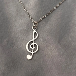 Halsband G-Klav Smycke Silver imitation - Så fint halsband med en g-klav. Trädd på kedja i silverimitation, justerbar 40-45 cm. Berlocken är ca 2,2 x 1 cm.  