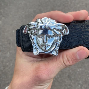 Svart Versace bälte med Medusa-spänne - Säljer ett svart Versace bälte i präglat skinn med ikoniskt Medusa-huvud i silver som spänne. Bältet har en lyxig känsla och sticker ut med sin detaljerade struktur och blanka spänne. Perfekt för dig som vill ha något extra till outfiten.äkta ny pris 4000