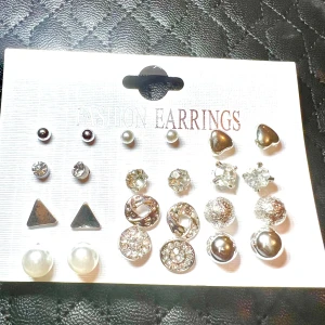 Set 12 par silverfärgade örhängen - Flera par örhängen i olika former som hjärtan, trianglar, pärlor och glittriga stenar. Färgerna går i silver, vitt och transparent. Perfekt för dig som vill variera din stil med både enkla och mer iögonfallande örhängen.