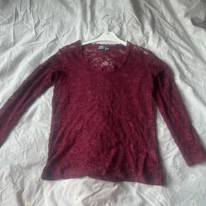 Blus - Säljer en vinröd blus i spets med lång ärm och rund halsringning. Blusen är genombruten med blommigt spetsmönster och har en feminin, elegant vibe. Perfekt för dig som gillar detaljer och vill sticka ut med en snygg topp i mörk röd ton.