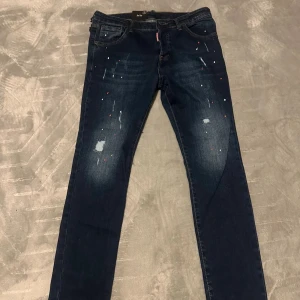 Dsquared2 mörkblå  jeans - Mörkblå skinny jeans från Dsquared2 med coola slitningar och färgstänk framtill. Klassisk femficksmodell med stor Dsquared2-logga bak i midjan. Jeansen har smal passform och är tillverkade i stretchig denim för extra komfort. Fick dessa i present och de passar ej mig!