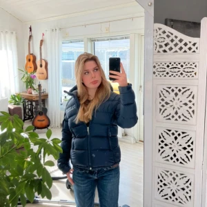 Mörkblå Peak Performance dunjacka XS - Säljer en mörkblå dunjacka från Peak Performance i storlek XS. Jackan har huva med snörning, två sidofickor med dragkedja och quiltad design. Perfekt för kalla dagar och har en clean, sportig look som funkar till jeans eller hoodie. Den är välanvänd och har därför ett litet hål på ena armen. Hålet gör ingen skillnad då du ändå kan tvätta den och det är så pass litet att det knappt syns.