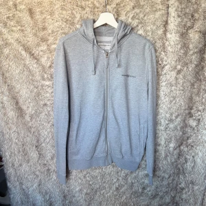 Grå hoodie från Henri Lloyd med dragkedja - Snygg ljusgrå hoodie från Henri Lloyd i mjuk bomullsblandning. Tröjan har huva med snörning, dragkedja framtill och diskret logga på bröstet. 