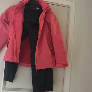 Rosa regnjacka från Didriksons - Säljer en snygg rosa regnjacka från Didriksons med huva och dragkedja. Jackan har justerbara ärmslut med kardborre och två stora fickor framtill. Perfekt för blöta dagar och håller dig torr med stil.