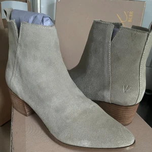 Helt nya, oanvända ljusgrå/beige stövletter i äkta mocka från K. Cobler! - Helt nya, oanvända stövletteri ljusgrå/beige mocka med naturfärgad sula och klack i läderfanér. Den spetsiga tån ger en nätt och feminin form. Innersulan i skinn ger en bra andningsfunktion och den 5 cm höga klacken är stabil och bekväm.