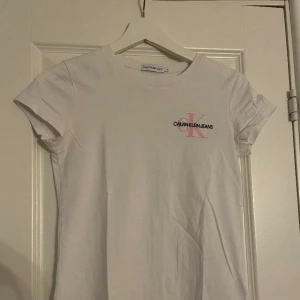 Calvin Klein T shirt  - En vit Calvin Klein T-shirt med rosa/svart märke. Använd få tal gånger. Storlek för 12-åringar, passar mig som en ganska smal o bär xss/xs.