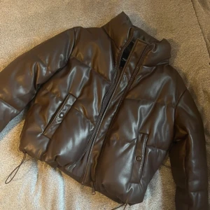 Jacka pull&bear - Superfin puffer från pull&bear, brunt PU material. Fint skick! Inte lika bomber aktig som på bild, utan den följer hela kroppen till rumpan. Passar mer XS