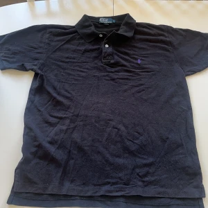 Polo piké svart - Säljer denna svarta pikétröja från Polo Ralph Lauren i storlek L. Loggan är i lila och tyget svart. Den är tillverkad av 100% bomull och är i mycket bra skick.