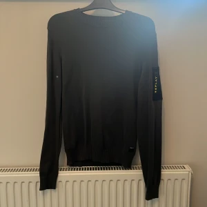 Grön tröja från Replay - En grön långärmad tröja från Replay. Tröjan har en enkel design med en ficka på ärmen som har en dragkedja och Replay-logotypen i gult.