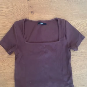 Brun topp från Bik Bok - En brun topp från Bik Bok med korta ärmar och en fyrkantig halsringning. Toppen är tillverkad i ett ribbat material och har en normal passform.