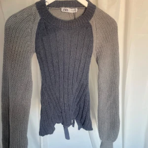 Grå stickad tröja från Zara - En blågrå stickad tröja från Zara med ribbad struktur på framsidan och ärmar i ett grövre stickat mönster. Tröjan har långa ärmar och en knytning i midjan. och är backless. aldrig någonsin använd 