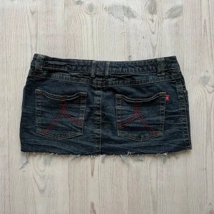 Lågmidjad mörkblå jeanskjol  - Mörkblå lågmidjad jeanskjol från Rainbow i fint skick som jag har gjort om från en längre kjol. Jag kan inte hitta storlek men skulle säga M. Tvärs över midjan är det 42 cm och längs med sidan är det 29 cm. Använd gärna köp nu!