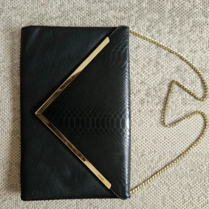Svart kuvertväska  - Svart stilren kuvertväskan med guld kant och guld färgad kedja.  33cm bred 21cm hög 39cm i diagonalt  Guld kedja på 80cm