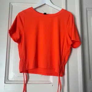 Orange tröja med band på sidorna som går att justera. 