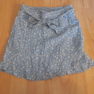 Kjol  - En kjol med shorts under. Kjolen är ljus blå med söta små vita blommor. Den har knyt funktion fram till och bak till så är den stretchig