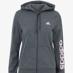 Upptäck Komfort och Stil: Adidas Fleecejackor För Alla Tillfällen! -  En Adidas fleecejacka i en snygg grå nyans. Den är tillverkad av mjukt och hållbart material som ger både värme och komfort. Jackan har en modern passform och är utrustad med praktiska fickor för förvaring av små föremål. 