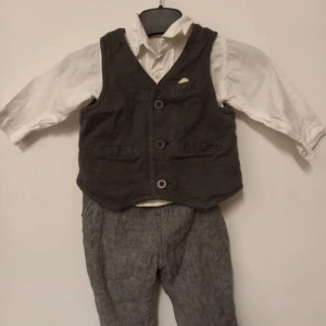 Finkläder ca strl. 68 - Vit skjorta av okänt märke, ca strl. 68, se mått på bild 2. I fint skick, utan fläckar och hål men saknar en knapp längst ner.  Grå väst samt grå linnefinbyxor från Next. Storlek 6-9 månader (9,5 kg), rymliga. I fint skick, inga hål eller fläckar 