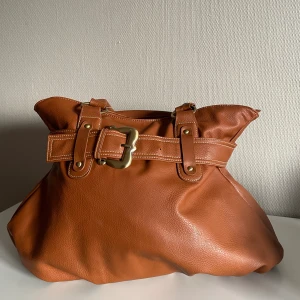 Brun rymlig väska för jobb, skola eller shopping 🛍️  - Söt och rymlig väska säljes💞 Med tre innerfack varav ett med kedja och ett litet fack på baksidan av väskan även med kedja så rymmer den mycket. Väskan är 38cm hög och 40cm som bredast i botten. Väskan är i fint skick!