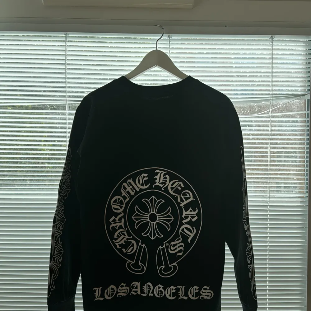 Denna långärmade tröja från Chrome Hearts är svart med vita detaljer och märkets logotyp på bröstfickan. Tröjan har dekorativa mönster längs ärmarna och är tillverkad av högkvalitativt material. Ett exklusivt plagg i utmärkt skick! Priset kan diskute. Hoodies.