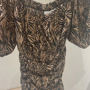 Mönstrad klänning - En mönstrad klänning med zebramönster i svart och beige. Klänningen har korta puffärmar och en åtsittande passform. jätte fin klänning som har använts 1 gång till ett bröllop. hör av dig ifall du är intresserad! 