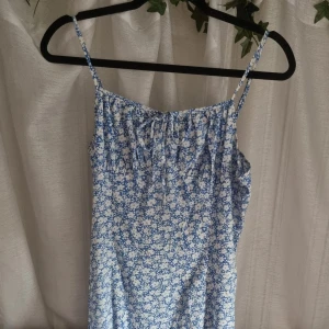 Blommig klänning  - Blå och vit blommig klänning. Inget stretch men sitter bra ändå. Dragkedja baktill och justerbara band. Snöre framtill för en liten detalj. En liten slits nertill. Strl. S, men passar XS också. 