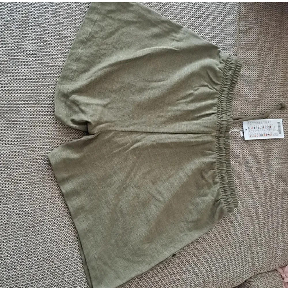 Ett par olivgröna shorts med elastisk midja och dragsko. Shortsen har två stora framfickor och är tillverkade i ett lätt och bekvämt material. oanvänd. 100% ny med pappret kvar i den.. Shorts.