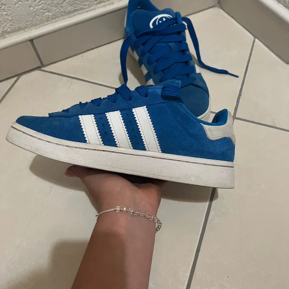 Snygga Adidas Campus sneakers i blått. Perfekt för vardagligt bruk eller träning. Skorna är lite använda och ser nästan nya ut. Har även box till skorna. Storleken på skorna är 38,5. De är pålitliga till storleken. Hör av dig vid frågor!. Skor.