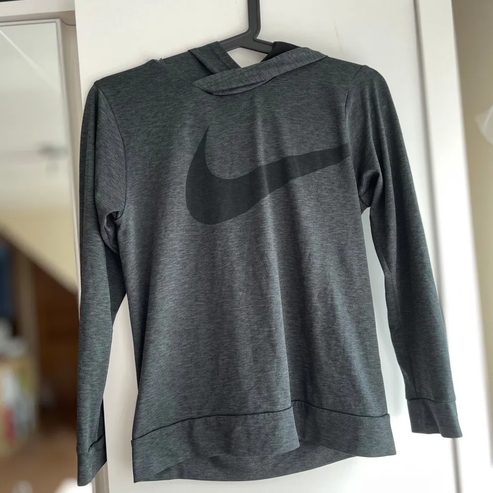 En grå hoodie från Nike med Dri-Fit teknologi. Tröjan har en stor Nike-logga på framsidan och är tillverkad i ett bekvämt och funktionellt material. Passar för barn i åldern 10-12 år, skulle säga att den motsvarar en XXS. Första bilden gör färgen rättvis. Sportswear.