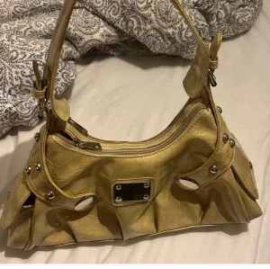 Y2k väska  - Ljus guldig y2k väska köpt second hand. Bra skick förutom att den är sönder på ett ställe ( bild 3) går att fixa. Jätte fin och hyfsat stor. Säljer för den inte kommer till användning 
