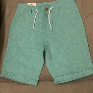 Turkos shorts  - Shorts i en ljus turkos färg med vita snören i midjan. Shortsen har två fickor framtill och två baktill.