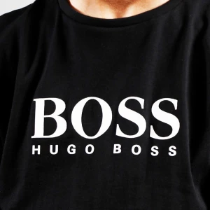 Riktig Boss Långärmad tröja - En stilren och bekväm svart långärmad tröja från Hugo Boss med vit text på bröstet. Tröjan har en normal passform och är tillverkad i ett mjukt material som passar perfekt för vardagsbruk.  Köpt för 1500 kr