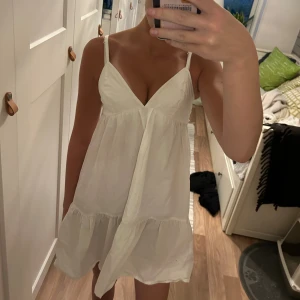 Vit klänning med volangdetaljer - En vit klänning med smala axelband och volangdetaljer. Klänningen har en v-ringad hals och snörning i ryggen. använd 1 gång på skolavslutningen💞 skriv om ni har några funderingar eller liknande😊