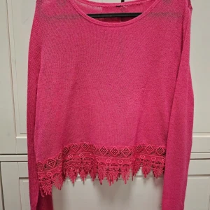 Rosa stickad tröja med spetsdetaljer - En rosa stickad tröja med långa ärmar och spetsdetaljer vid nederkanten. Tröjan har en rund halsringning och är i ett lätt och bekvämt material.