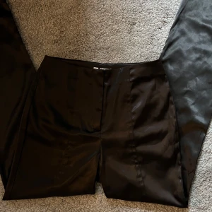 Glansiga Kostymbyxor NA-KD - Glansiga kostymbyxor från NA-KD i storlek 36. Byxorna har använts några fåtal gånger.