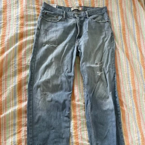Levi's 550 Relaxed Fit Jeans - Ett par ljusblå Levi's 550 jeans med avslappnad passform. Byxorna har slitna detaljer på framsidan och baksidan, samt en klassisk femficksdesign. De är tillverkade i jeansmaterial och har en knapp- och dragkedjestängning.