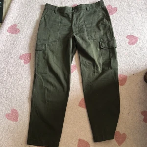 Army Grön Cargo Byxor - Army gröna cargo byxor köpta på loppis och aldrig använda, det står ingen storlek men skulle säga att de är large i midjan och sen medium/small i benen, varning att de är ganska smala i benen men stora i midjan.